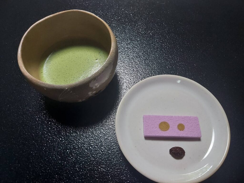 一休寺さんで出していただいた抹茶とお菓子、一休寺納豆。黒いお盆の上に、抹茶の入った茶碗と白い皿が並んでいます。